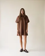 Vestido corto color marrón de lino, con silueta amplia y relajada, cuello fruncido y mangas cortas abullonadas.