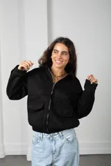Campera de gamuza negra con cierre frontal, cuello camisero, bolsillos delanteros con solapa y puños con botón.