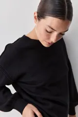 Sweater negro de tejido suave con escote redondo, mangas largas y calce relajado, con terminaciones acanaladas en cuello, puños y ruedo.
