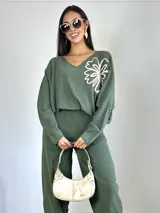Sweater de punto oversized color verde, con escote en V y manga larga. Presenta un aplique bordado en forma de flor en el hombro izquierdo.
