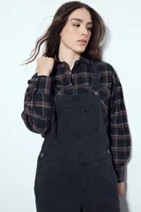 Camisa tipo leñadora de corte oversize, con estampado de cuadros en tonos negro y marrón. Presenta cuello clásico, cierre frontal con botones y mangas largas con puños abotonados.