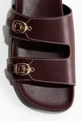 Sandalias H&M color bordó, de diseño abierto con dos tiras anchas en el empeine, cada una equipada con una hebilla metálica dorada y costuras pespunteadas en contraste. Plantilla anatómica.