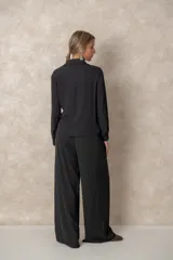 Camisa de corte clásico con cuello camisero, mangas largas con puños abotonados y cierre frontal con botones. Presenta un diseño con lazo ajustable integrado en la cintura que permite entallar la prenda.