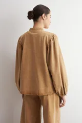 Camisa de jean color camel, de manga larga abullonada, con cuello mao y cierre frontal de botones metálicos.