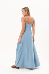 Vestido largo de denim fino y liviano, color celeste, con breteles finos, escote delicado, silueta entallada en la parte superior, falda amplia con recortes verticales y bolsillos laterales.