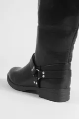 Bota alta de cuero sintético negro, con taco bajo, puntera redondeada y detalles de tiras con hebilla y tachas metálicas en el tobillo.