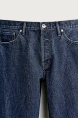 Jeans regular fit de tiro medio, confeccionados en denim de algodón azul oscuro con efecto lavado. Presenta diseño clásico de cinco bolsillos, pierna recta y cierre frontal con cremallera y botón.