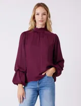 Blusa Tahari de gasa satén color violeta oscuro, con cuello alto fruncido y mangas largas abullonadas. La espalda tiene una abertura central con cierre de botón.