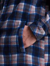 Sobrecamisa de tejido polar con estampado abstracto en tonos rojizos y azul marino. Presenta cuello clásico, cierre frontal con botones a presión, dos bolsillos frontales con solapa en el pecho y un parche decorativo.