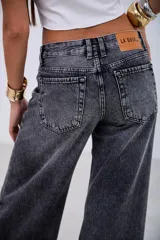 Pantalón de jean estilo wide leg en color negro con efecto lavado. Presenta un corte holgado, tiro medio y costuras reforzadas a lo largo de las piernas, con un ruedo deshilachado y desgastado.