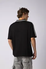 Remera tipo chomba tejida de algodón color negro, con cuello en V y mangas cortas. Presenta detalles de rayas blancas en cuello y mangas, y estampados con logos en el frente.