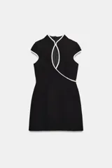 Vestido corto negro con cuello mao, abertura en el pecho y ribetes blancos en contraste. Cuenta con mangas cortas y cierre lateral con cremallera oculta.