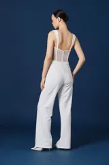 Mono largo color blanco de la marca Natalia Antolín, con diseño strapless con tirantes, cuerpo estilo corset de encaje semitransparente con ballenas visibles y parte inferior de pantalón recto de vestir.