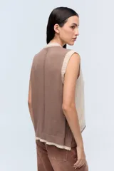 Chaleco de punto color beige con escote en V y ribete blanco.