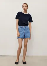 Short de denim azul medio, de tiro alto y diseño recto con cinco bolsillos, trabillas para cinto y cierre frontal con cremallera y botón.