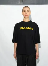 Remera negra de corte holgado con mangas cortas y estampado frontal con la palabra "ideales" en color amarillo.