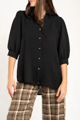 Blusa negra de corte oversize, con cuello camisero, cierre frontal de botones y mangas tres cuartos con terminación elástica.
