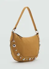 Bolso de hombro tipo hobo en color tostado, confeccionado en piel bovina con acabado de gamuza. Presenta un diseño semicircular decorado con tachuelas metálicas plateadas en el contorno inferior y cierre de cremallera superior.