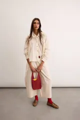 Camisa de algodón color crudo, con calce relajado, cuello clásico, botones delanteros, mangas largas con sutil volumen y ruedo asimétrico.