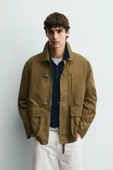 Parka de corte relajado confeccionada en mezcla de algodón color marrón. Presenta cuello solapa, cierre frontal con cremallera oculta y alamares metálicos, bolsillos de plastrón con solapa en la cadera y bolsillo de vivo en el pecho.
