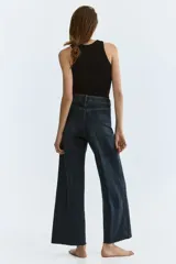 Jean tobillero de denim azul con leve elasticidad, tiro alto y perneras amplias tipo wide leg. Presenta bolsillos delanteros tipo parche con solapa y botones metálicos, además de pliegues marcados al frente y en la espalda.