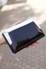Billetera grande de cuero charol negro con borde superior blanco y cierre con cremallera.