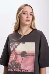 Remera de manga corta oversize color gris oscuro con estampa fotográfica de palmeras y edificio rosado.