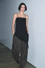 Top negro con estampado de lunares blancos, escote recto, tirantes finos, detalle de encaje en el escote y bajo asimétrico con abertura lateral.