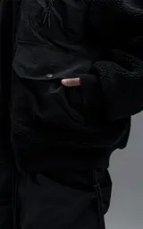 Campera estilo bomber unisex, confeccionada en una combinación de corderito sintético y paneles de ripstop. Presenta un diseño utilitario con múltiples bolsillos frontales con cierres y broches a presión, cuello, puños y ruedo en ribb elástico.