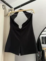 Catsuit corto negro, ajustado al cuerpo, con escote pronunciado en V y detalle de cierre metálico en forma de V en el centro del busto.