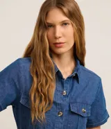 Vestido midi de jean con cuello camisero, manga corta y cierre frontal con botones. Cuenta con bolsillos frontales con solapa en el pecho, bolsillos laterales en la falda y cinturón ajustable con hebilla redonda carey.