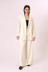 Blazer color crema con solapas de muesca, cierre frontal con dos botones, bolsillos delanteros con solapa y mangas largas con bordados calados.