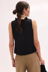 Top sin mangas color blanco con escote en V y volados en el cuello y la botonera delantera.