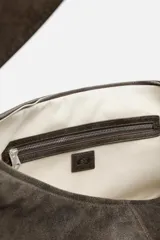 Bolso de hombro tipo media luna, fabricado en piel craquelada color marrón oscuro. Tiene un compartimento principal con cierre de cremallera y un bolsillo interior también con cremallera.