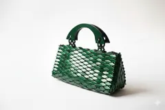 Cartera de mano verde, con diseño texturizado en relieve similar a escamas y asas rígidas de madera.