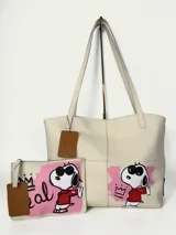 Tote bag de cuero color natural con diseño intervenido a mano por la artista GGIL, presentando a Snoopy con gafas de sol y corona. Incluye un sobre a juego con el mismo diseño artístico. Posee doble asa de hombro y diseño sin forro.