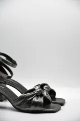 Sandalia de tacón medio ancho con diseño de nudo frontal y pulsera ajustable al tobillo con hebilla metálica.