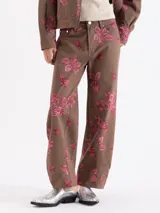 Pantalon de corte recto y tiro medio, confeccionado en tela color marrón con estampado de fresas y hojas en tono rosado. Cuenta con cierre frontal y bolsillos laterales.