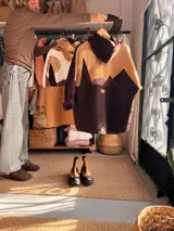 Campera con capucha de diseño patchwork, confeccionada en tejido tipo corderito en tonos marrón y tostado. Presenta un diseño que simula un paisaje montañoso con cortes irregulares y etiqueta de marca en la parte posterior.