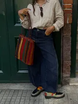 Cartera tipo tote de cuero con diseño de franjas verticales multicolores en tonos tierra, rojo y azul. Cuenta con correas trenzadas de cuero y cierre superior.