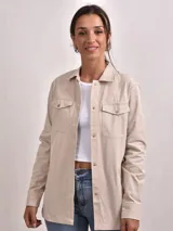 Camisa color beige con cuello clásico, cierre frontal con botones, dos bolsillos con solapa en el pecho y mangas largas con puños abotonados.