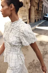 Blusa de manga corta abullonada con diseño a cuadros, cuello con volante y acabados elásticos. Cuenta con aberturas y lazos ajustables en los laterales.