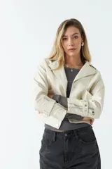 Campera de cuero sintético en color crema, con diseño ajustado al cuerpo y largo hasta la cintura. Presenta cierre frontal con botones, bolsillos con solapa y detalles de cierres metálicos en los puños.