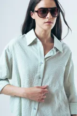Camisa de corte oversize en color gris oscuro, confeccionada en tejido con textura acanalada. Presenta cuello clásico, cierre frontal con botones y mangas largas con puños.