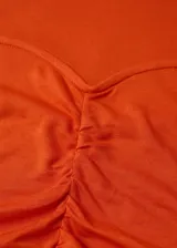 Camiseta de manga larga color naranja, con cuello redondo y diseño entallado. Presenta un detalle fruncido central y costuras decorativas en el frente.