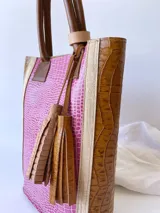 Bolso matero de cuero color fucsia y marrón con textura croco, doble asa de mano marrón y detalle de borlas de cuero marrón.