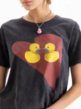 Remera gris oscuro con efecto acid wash, corte clásico, mangas cortas y cuello redondo. Cuenta con una estampa frontal de un corazón rojo con dos patitos amarillos besándose.
