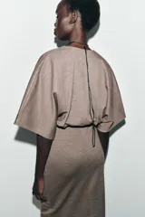 Vestido midi de tejido piqué en color marrón oscuro jaspeado, con escote en pico cruzado y mangas cortas. Presenta detalle de frunces en la cintura y un cinturón integrado con hebilla metálica a contraste.
