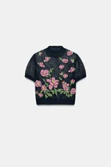 Top de punto calado color azul marino, con cuello subido y manga corta. Presenta un diseño con flores bordadas en tonos rosados y verdes en la parte delantera.