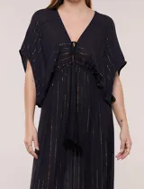 Vestido largo negro confeccionado en gasa con hilos de lurex en relieve vertical. Presenta escote en V profundo con lazo frontal y borlas, mangas holgadas tipo kimono, cintura elastizada y falda fluida con ruedo con volante.